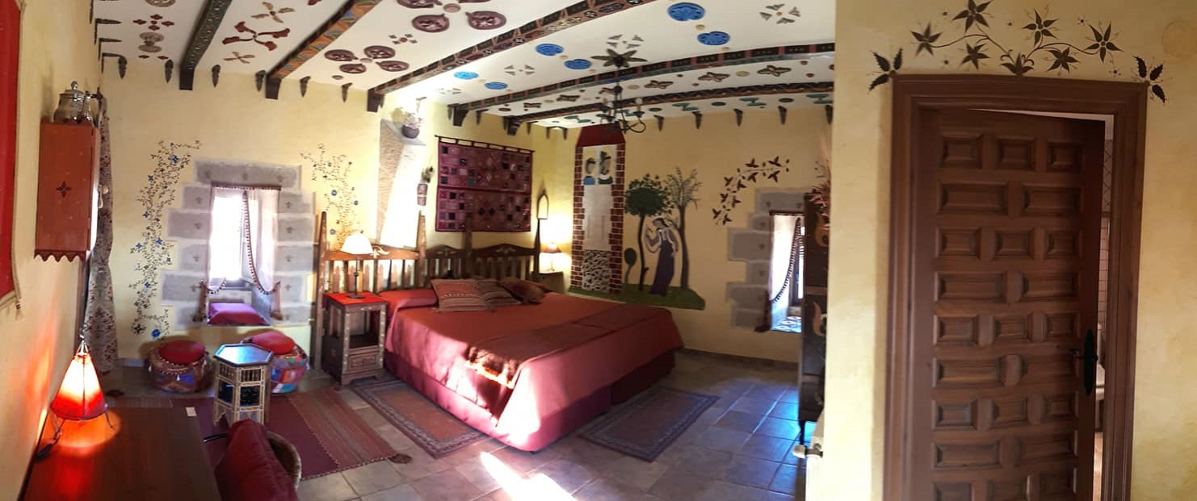 A bedroom with a large bed, a wooden door, and a ceiling with decorative patterns.