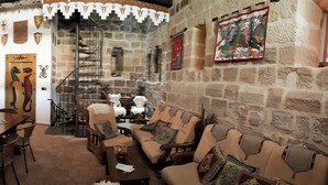 A cozy, stone-walled dining area with a wooden table and chairs, surrounded by various decorative items and a staircase leading to an upper level. - TORRE FUERTE S.XIII (Baños de Rioja)
