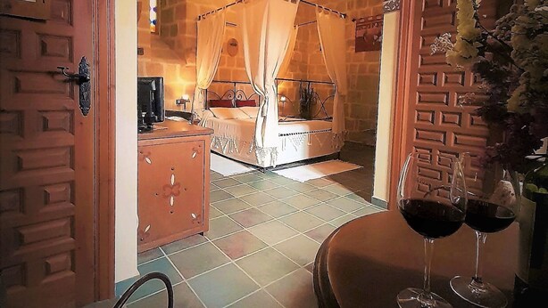 A cozy bedroom with a canopy bed, a wooden door, and a dining area with two wine glasses. - TORRE FUERTE S.XIII (Baños de Rioja)