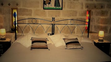 Una cama con cabecera de metal, dos mesitas de noche con lámparas y una ventana con vidrieras.