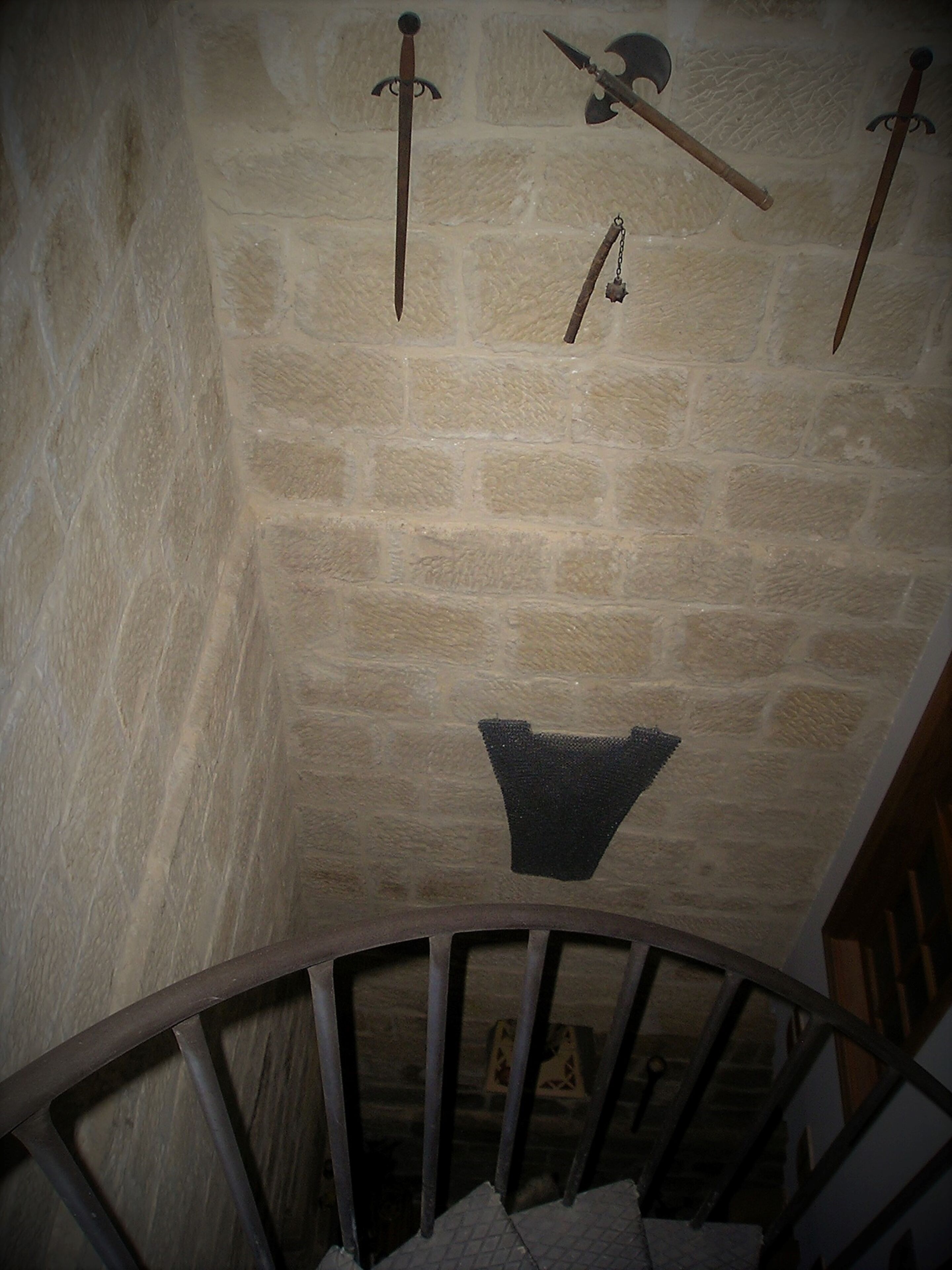Una habitación con paredes de piedra, una escalera de madera y un perchero colgante.