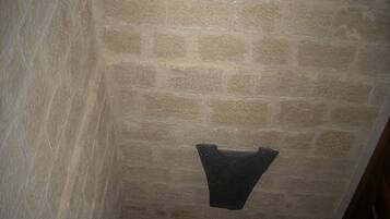 Una habitación con paredes de piedra, una escalera de madera y un perchero colgante.