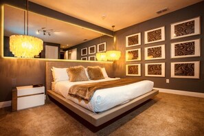 A modern bedroom with a large bed, a bedside table, a mirror, and a chandelier.