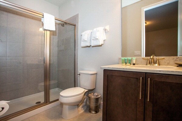 A bathroom with a glass-enclosed shower, a toilet, and a sink with a marble countertop.