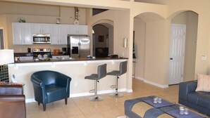 A modern kitchen with white cabinets, a central island with bar stools, a blue leather chair, and a sofa with cushions. - Ip60527 - Sand Hill - 4 Bed 3 Baths Villa (Davenport)