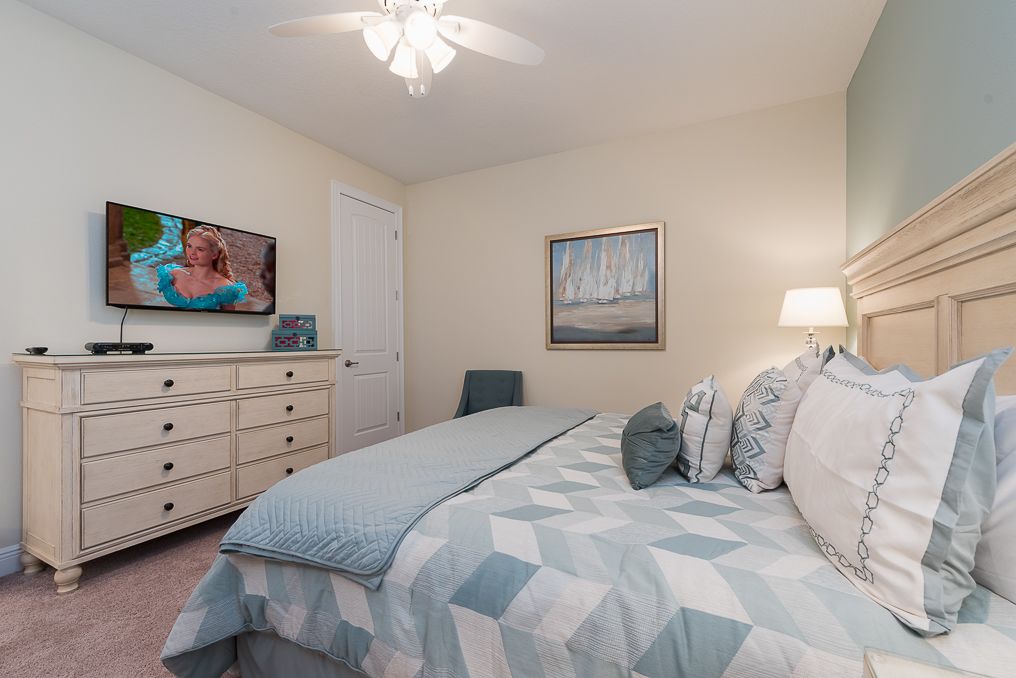 A bedroom with a bed, a dresser, a television, and a painting on the wall.