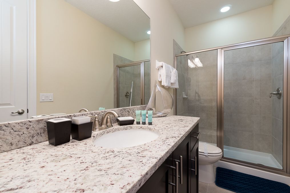 A bathroom with a granite countertop, a sink, a mirror, a shower enclosure, and a toilet.