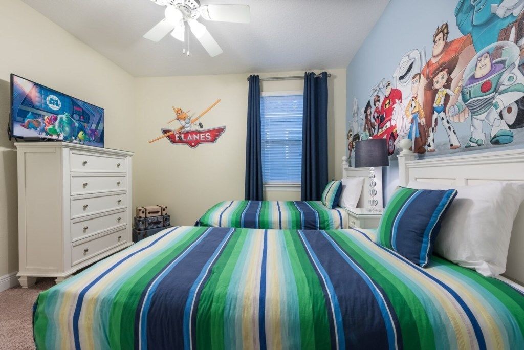 A bedroom with a striped bedspread, a ceiling fan, a TV, and a wall mural.