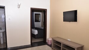 Ein Hotelzimmer mit Bett, Wand-Fernseher, Holzkonsolentisch, Mülleimer und Badezimmer mit Waschbecken und Toilette.