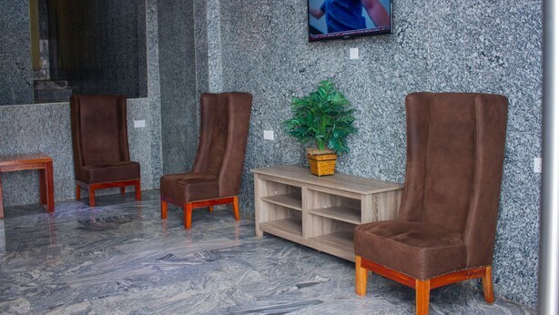 Eine Lobby mit drei braunen Ledersesseln, einem Holztisch, einem an der Wand montierten Fernseher und einem Blumentopf auf einer Holzkonsole.