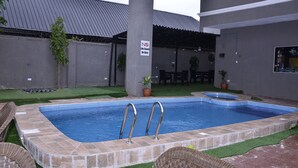 Ein Swimmingpool mit zwei Leitern, umgeben von künstlichem Gras und Korbmöbeln.
