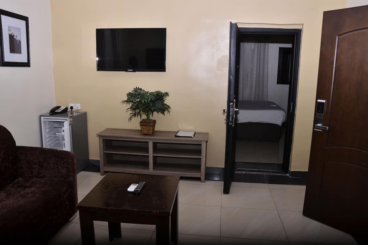 Ein Hotelzimmer mit einem Bett, einem an der Wand montierten Fernseher, einem kleinen Tisch mit Fernbedienung, einer Couch und einer Zimmerpflanze.