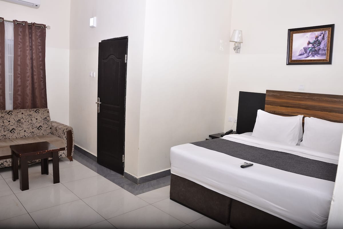 Ein Hotelzimmer mit Bett, Sofa, kleinem Tisch, einer Tür und einer Wandlampe.