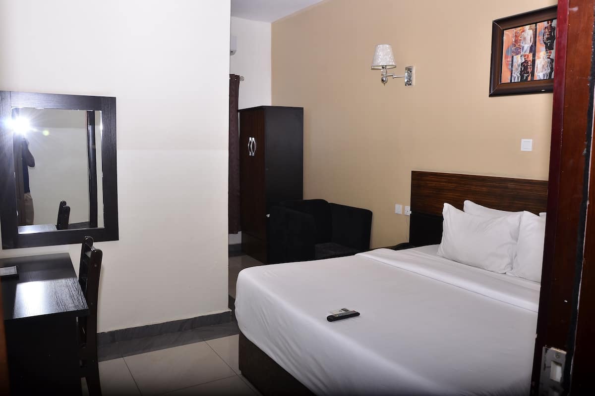 Ein Hotelzimmer mit einem Bett, einem Schreibtisch, einem Stuhl, einem Kleiderschrank und einer Wandlampe.