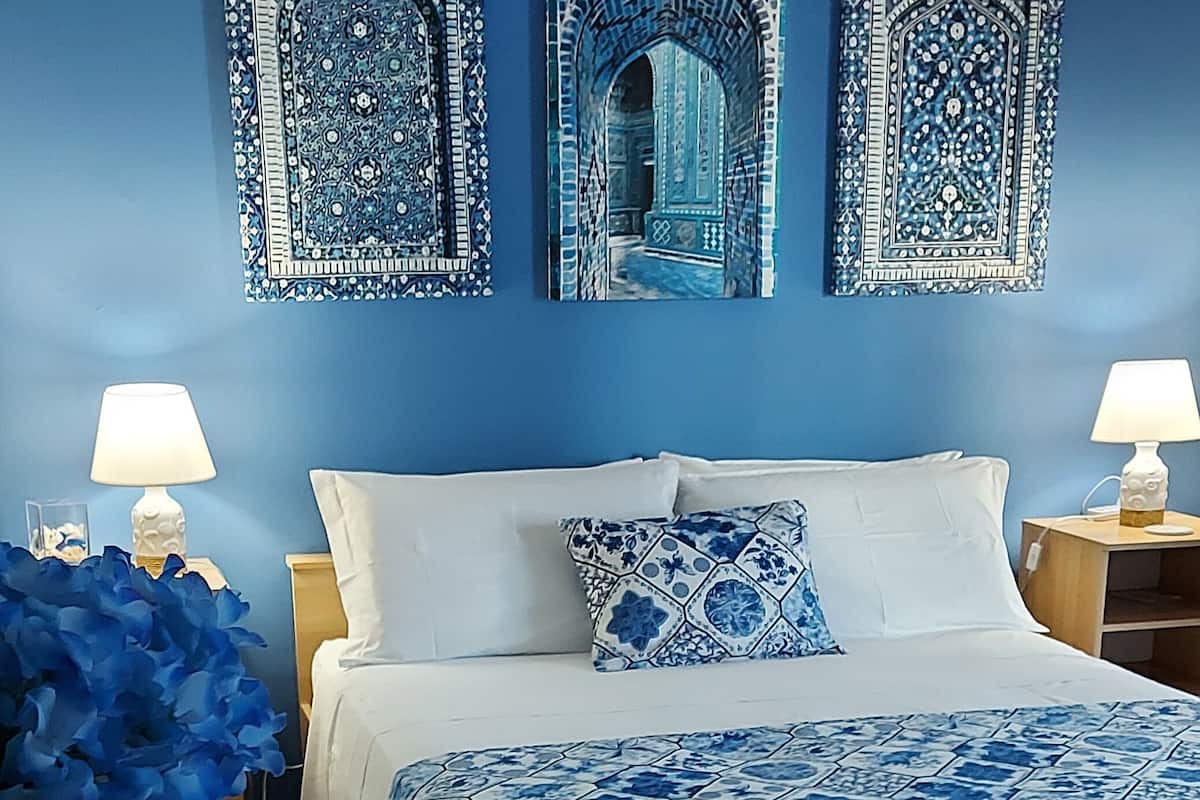 A bedroom with a bed, two nightstands, a blue wall, and three decorative wall pieces.