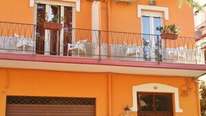A building with an orange facade, a balcony with a metal railing, and a closed garage door. - Casa Del Sole Accomodation (Tropea)