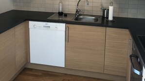 Una cocina moderna con armarios de madera, encimera negra, lavavajillas Bosch y pileta de acero inoxidable.