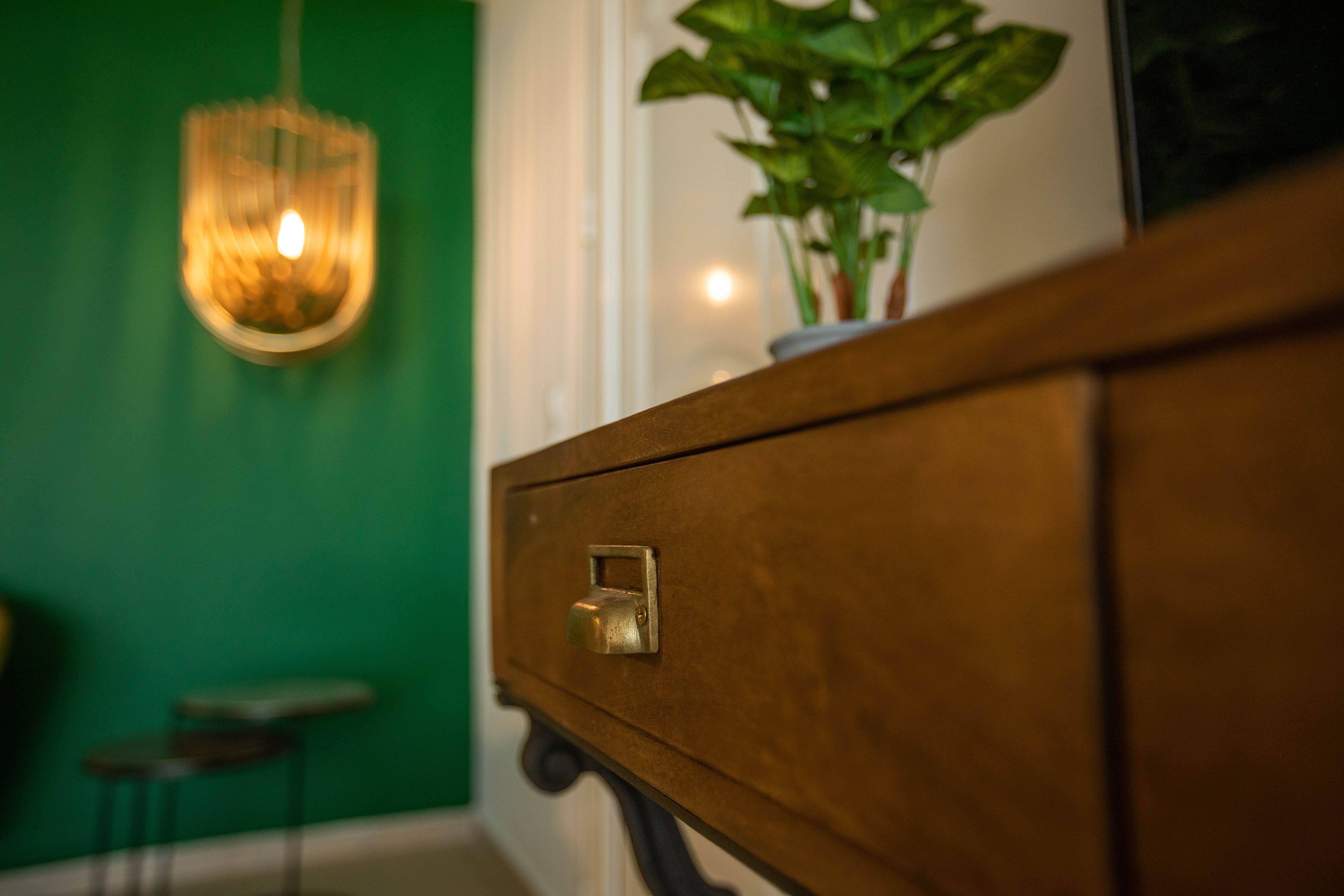 A wooden cabinet with a brass handle, a green wall, and a hanging light fixture.