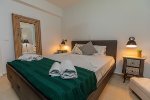 A neatly made bed with a green blanket, two white towels, and a wooden headboard. There are two bedside tables with lamps and a small plant. - Villa Serenity (Kefalonia)