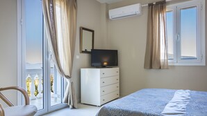 Un dormitori amb un llit, una petarrera, una televisió i una finestra amb cortines.