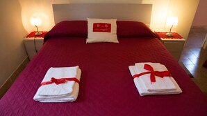 A neatly made bed with red bedding, two pillows, and two folded towels with red ribbons. - La Loggetta (Bagnoregio)