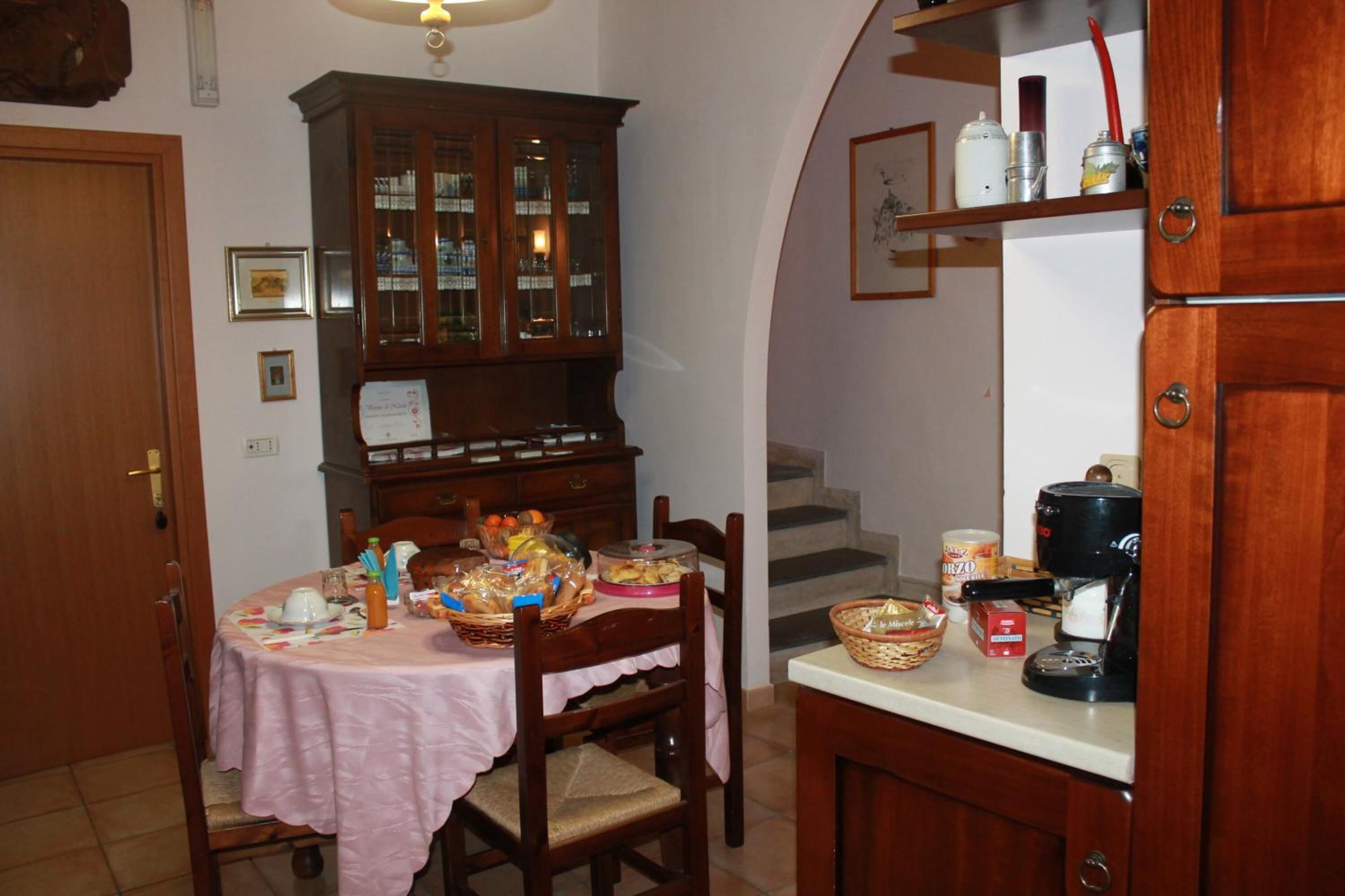 A dining area with a table set for two, a wooden cabinet with glass doors, and a kitchen counter with a coffee maker.