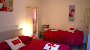 Habitación de hotel con dos camas, cada una con ropa de cama roja y almohadas blancas, una silla de madera y obras de arte en las paredes.