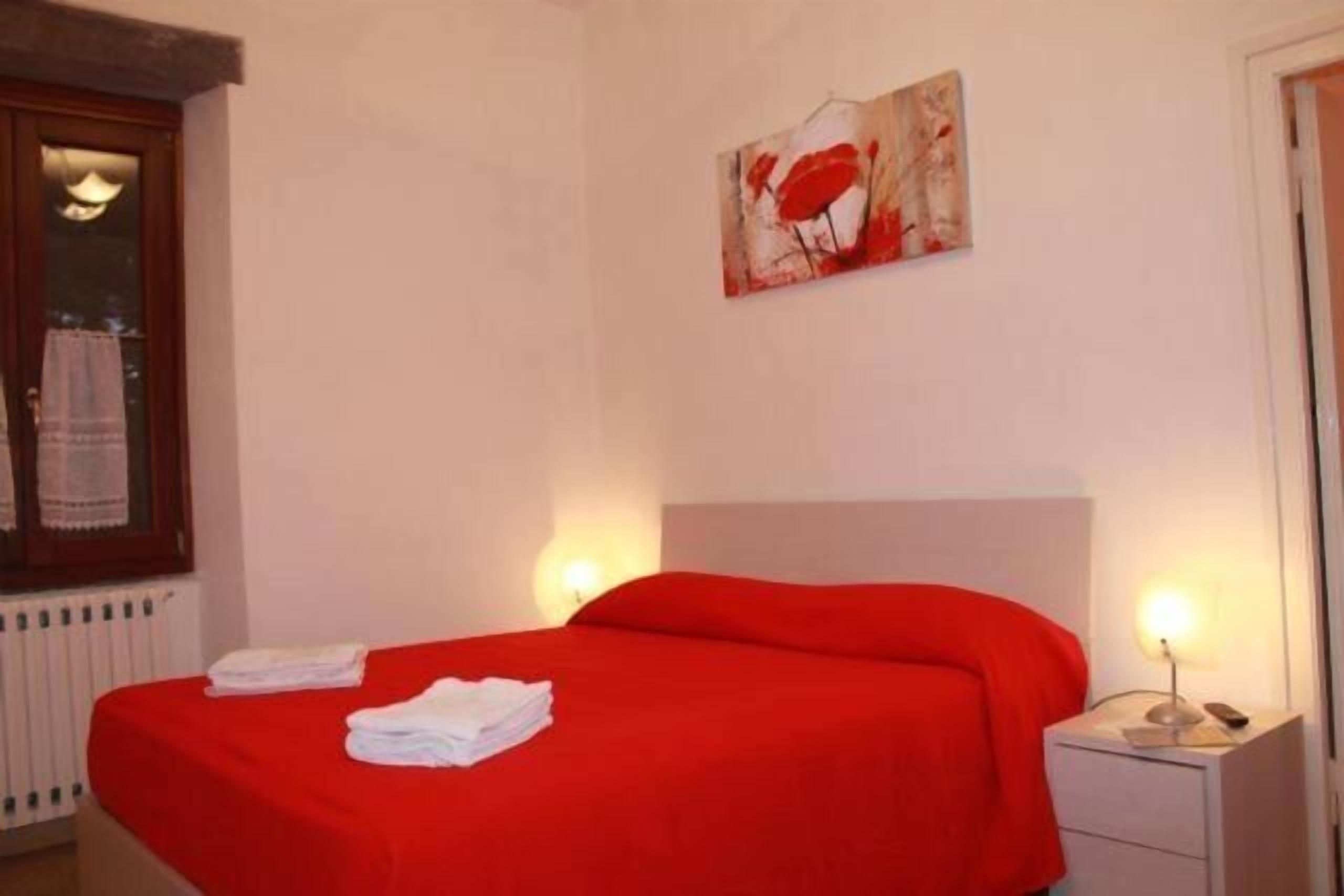 Quarto de hotel com cama, mesa de cabeceira, pintura na parede e janela com cortina.
