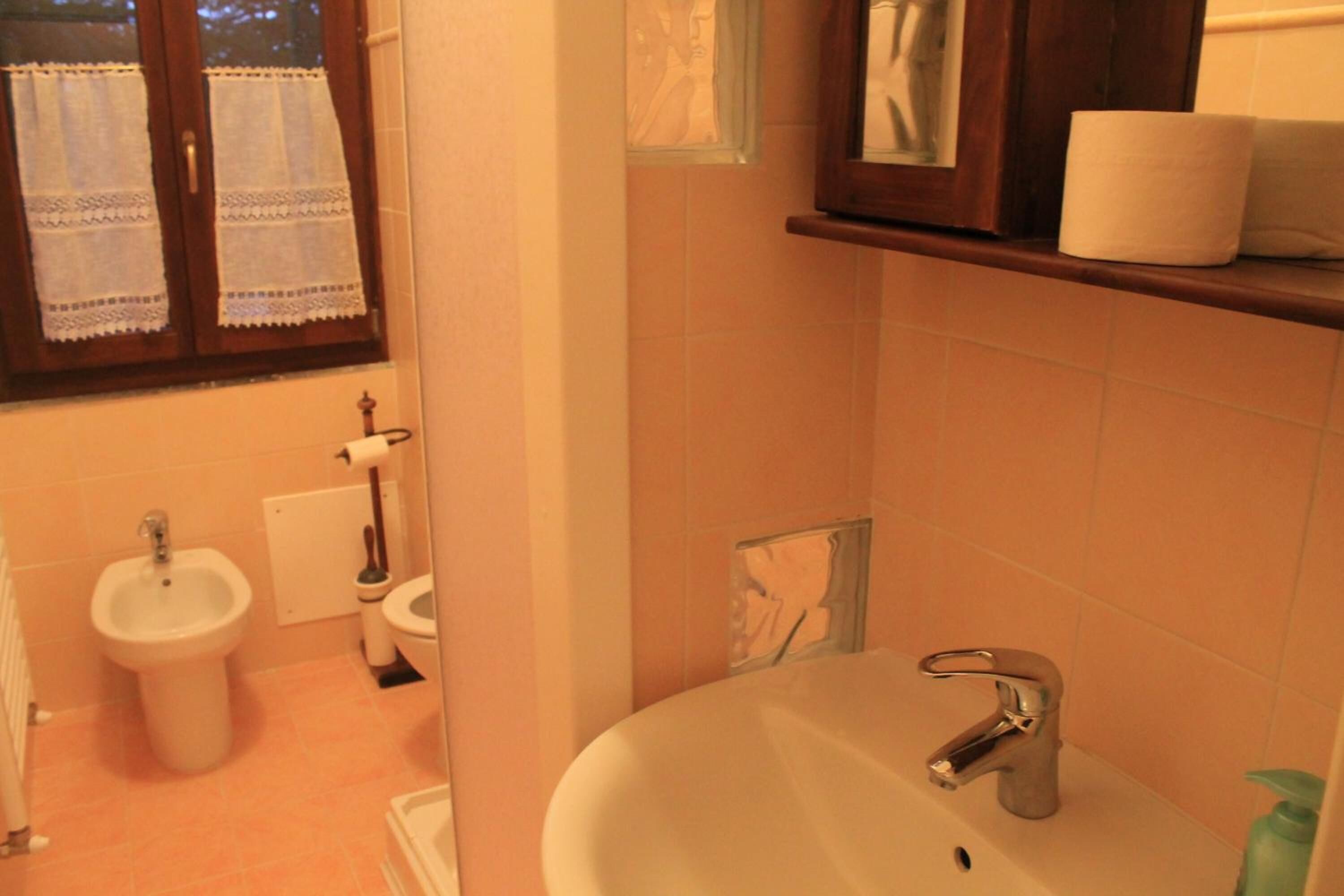 Une salle de bain équipée d’un lavabo, de toilettes, d’un bidet et d’une fenêtre ornée de rideaux en dentelle.