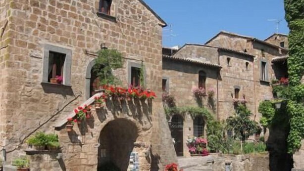 A stone building with an arched entrance, potted plants, and a cobblestone street. - La Loggetta (Bagnoregio)