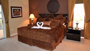 A bedroom with a large bed, two bedside lamps, a nightstand, a framed picture on the wall, and a window with curtains. - Ip60471 - The Shire at West Haven - 5 Bed 3 Baths Villa (Davenport)