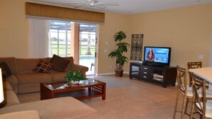 A living room with a sofa, coffee table, TV, and dining area. - Ip60471 - The Shire at West Haven - 5 Bed 3 Baths Villa (Davenport)