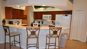 A kitchen with a central island, wooden bar stools, a microwave, a refrigerator, and a trash can. - Ip60471 - The Shire at West Haven - 5 Bed 3 Baths Villa (Davenport)