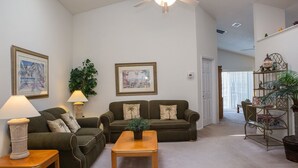 A spacious living room with a high ceiling, a ceiling fan, two couches, a wooden coffee table, and a bookshelf. - Ip60195 - Hampton Lakes - 3 Bed 2 Baths Villa (Davenport)