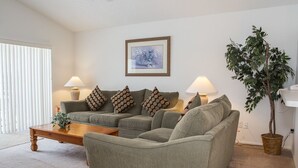 A living room with a sectional sofa, two side tables with lamps, a framed picture on the wall, and a potted plant. - Ip60195 - Hampton Lakes - 3 Bed 2 Baths Villa (Davenport)