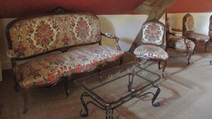A room with a wooden ceiling, a floral sofa, two armchairs, and a glass coffee table. - La Ferme du Grand Launay (Semblancay)