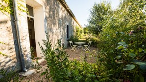 A rustic stone building with a garden patio featuring a table and chairs. - La Ferme du Grand Launay (Semblancay)