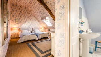 A bedroom with two beds, a small window, a bedside table, and a nightstand.