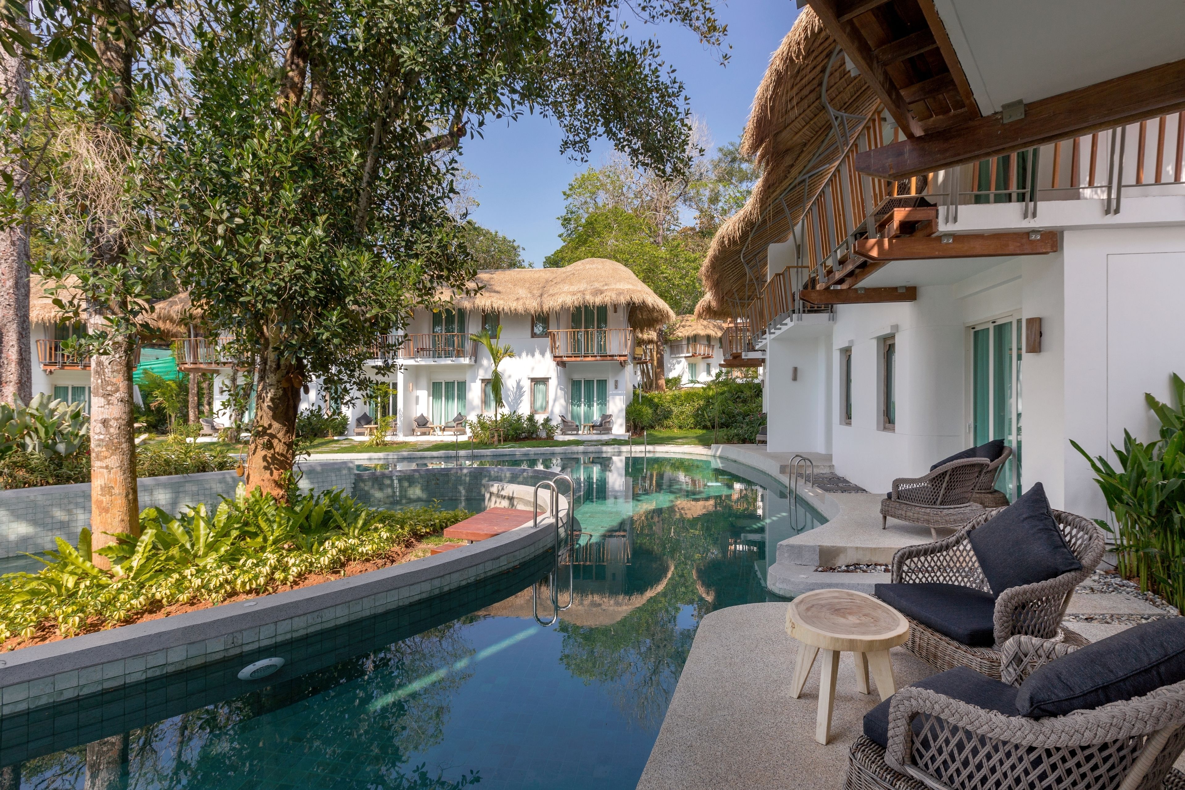 A pool area with a clear view of the pool, lounge chairs, and a building with a thatched roof.