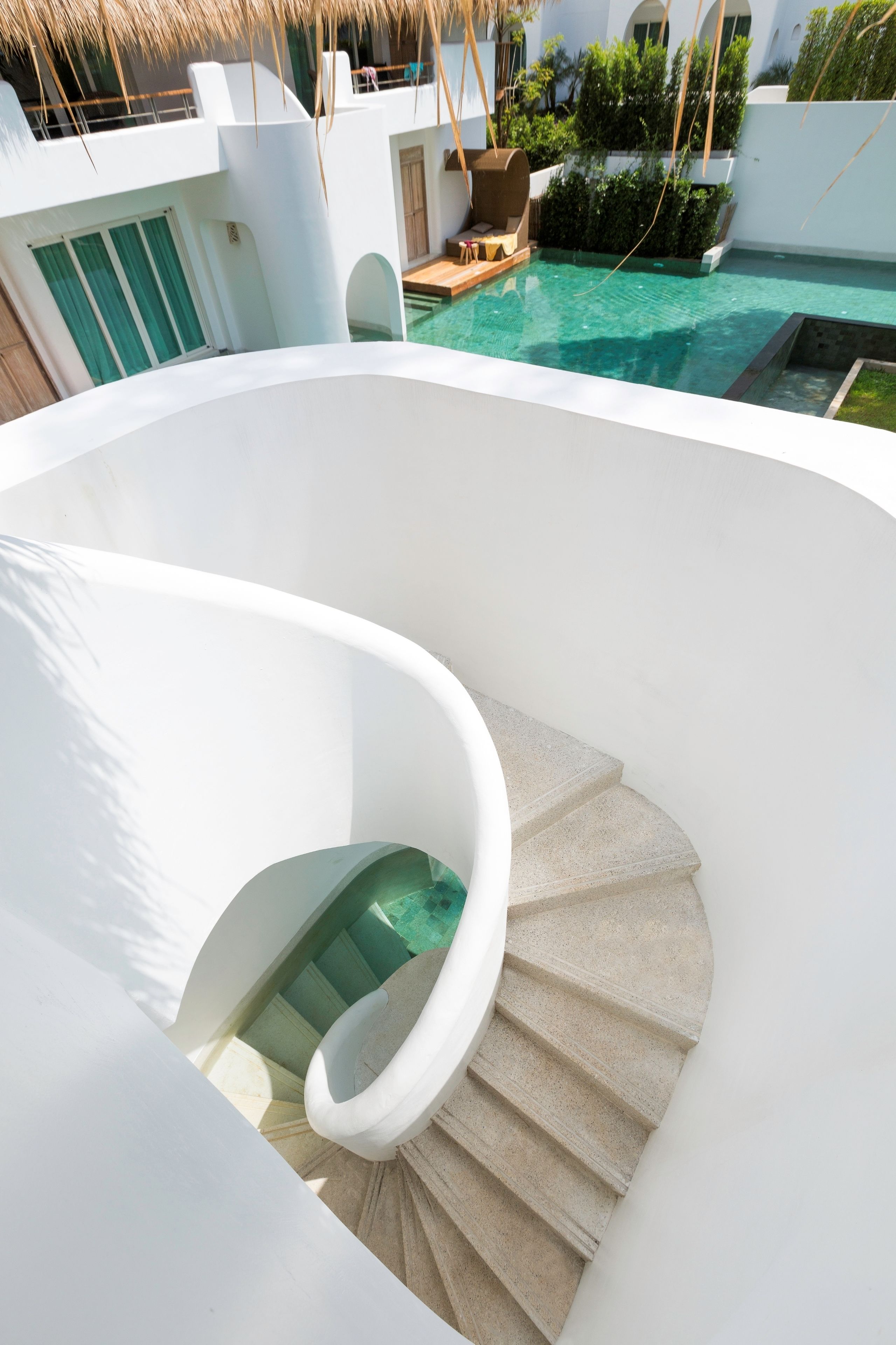 A spiral staircase leading to a pool area with a clear view of the pool and surrounding greenery.