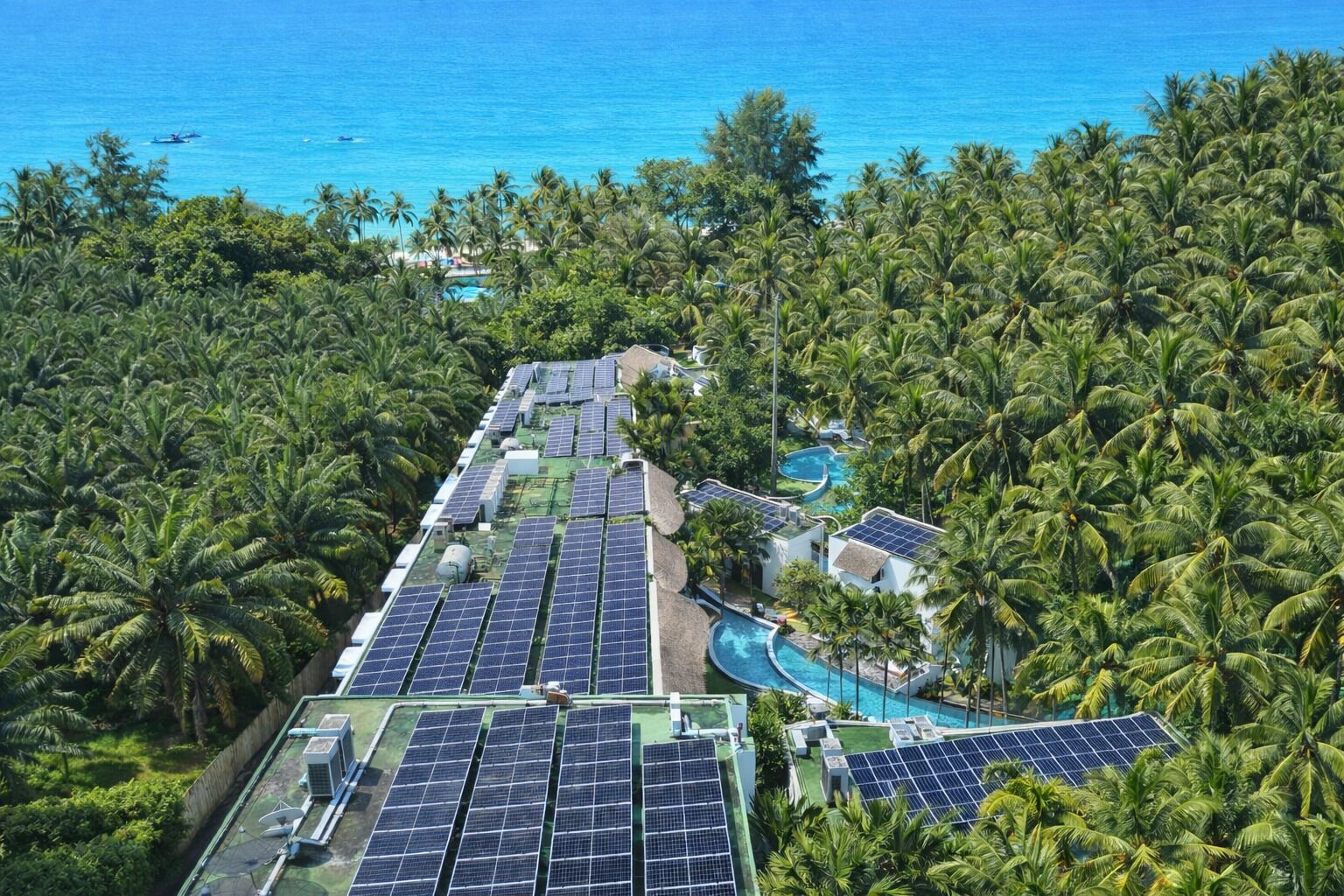 A resort with solar panels, swimming pools, and dense palm trees.