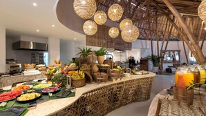 Un espace buffet proposant divers plats et boissons, une cuisine à l’arrière-plan et un plafond en bambou.