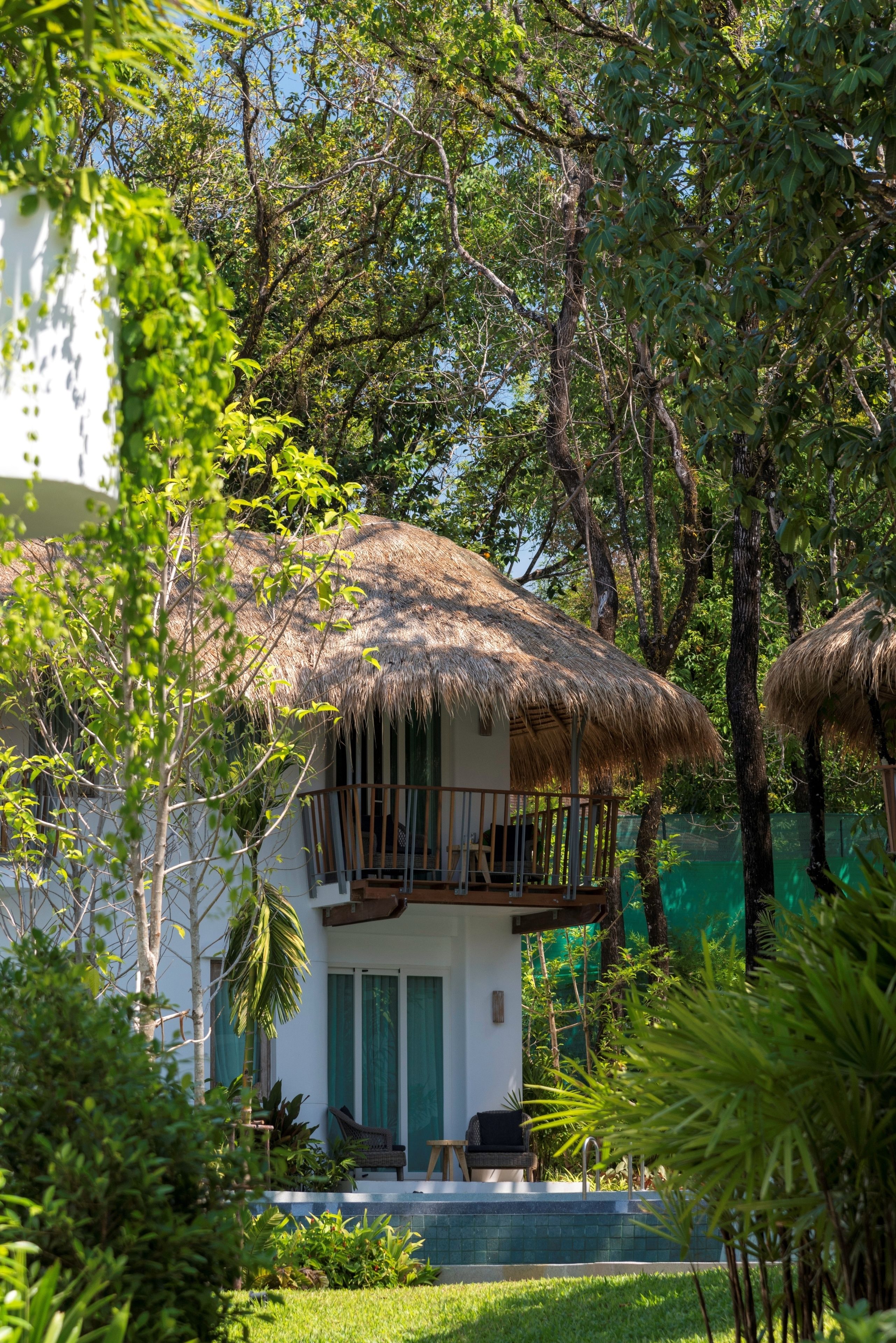 A house with a thatched roof, surrounded by lush greenery and trees.