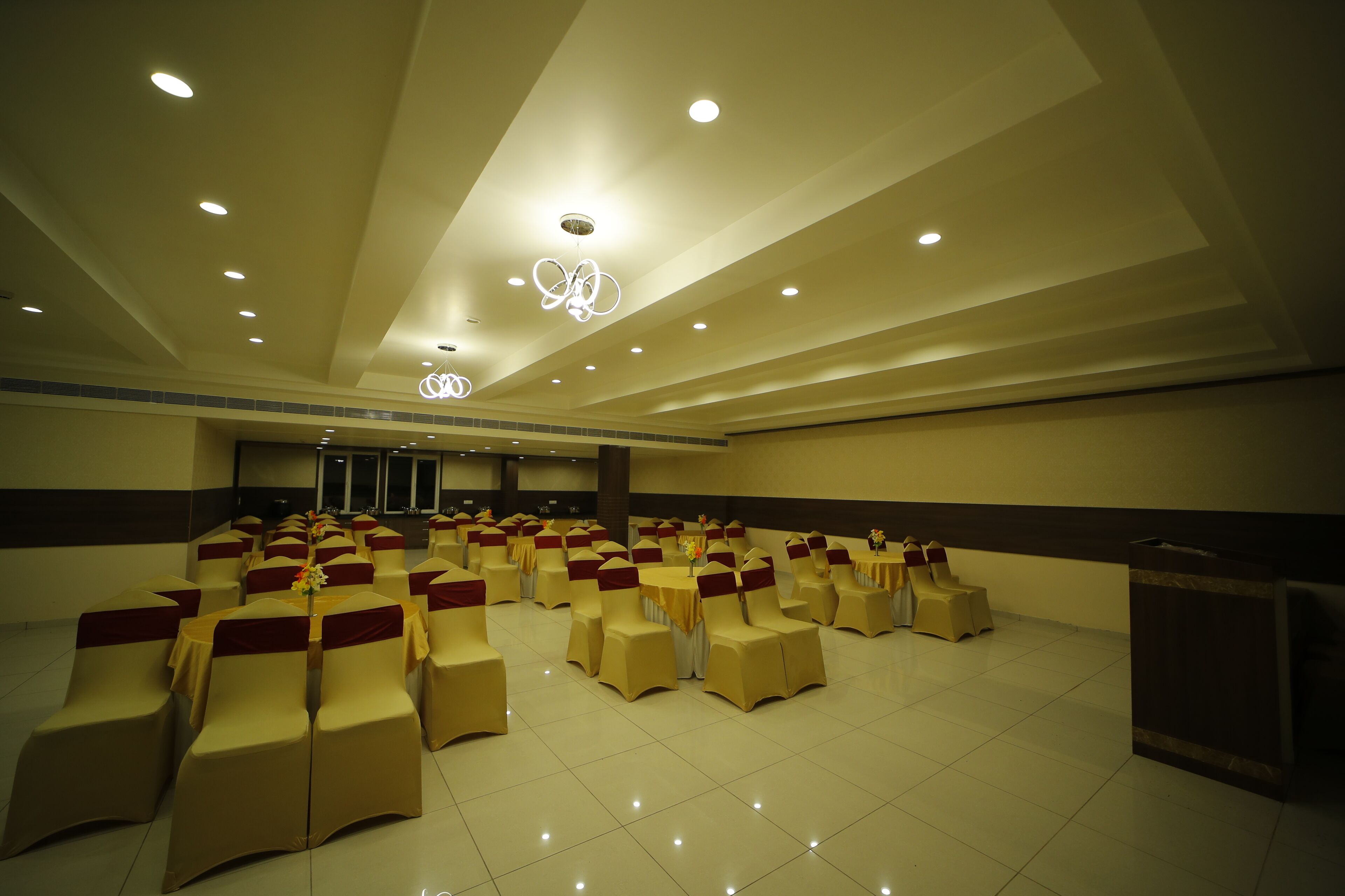 A spacious hall with rows of chairs and tables, recessed lighting, and a decorative ceiling feature.