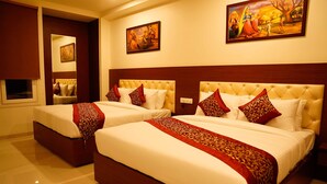 Habitación de hotel con dos camas, cada una con una colcha de diseño rojo y dorado, cabeceros de madera y un cuadro sobre las camas.