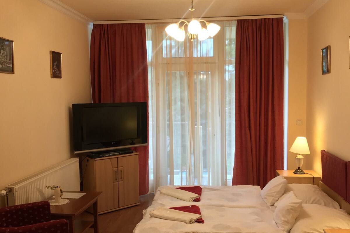 Una habitación de hotel con cama, televisión, escritorio, silla, lámpara y ventana con cortinas.