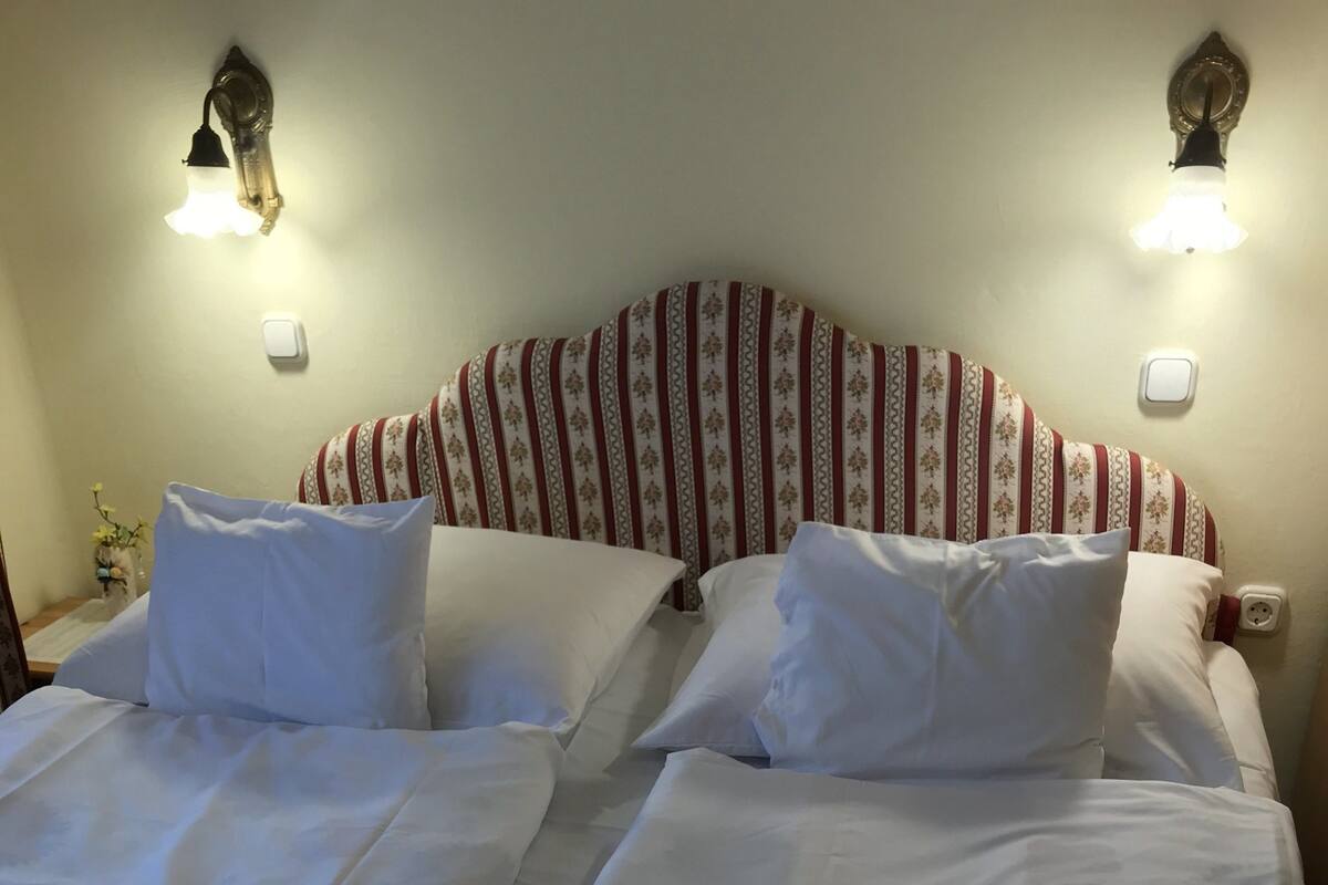 Habitación de hotel con dos camas, cada una con ropa blanca y toallas rojas. Hay lámparas de pared sobre las camas.