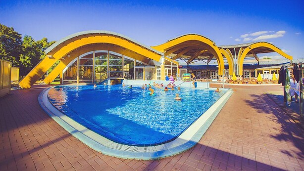 Une piscine dotée d’une structure de toit incurvée, entourée d’un chemin piétonnier en briques.