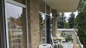 Un balcon avec des chaises et des tables en plastique blanc, un mur en briques et une porte vitrée.