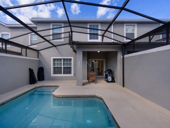 A swimming pool with a covered patio area, a door leading to a covered entryway, and a building in the background.